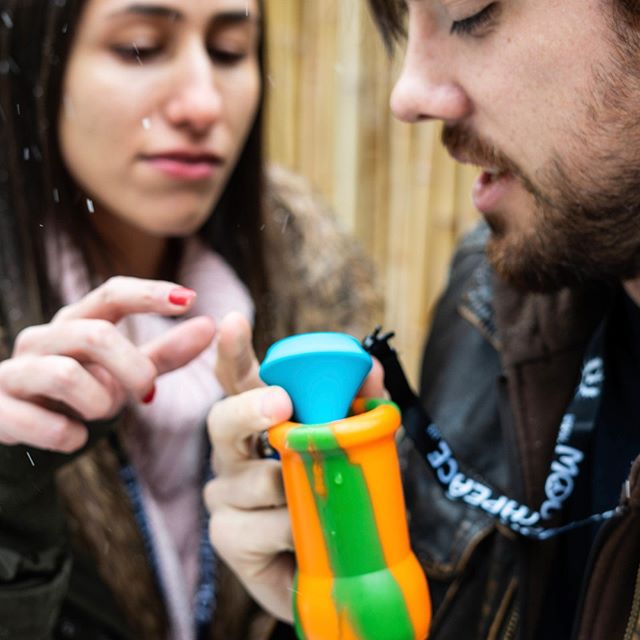 A person holding a bright orange and green silicone bong with a blue bowl piece while cleaning it.