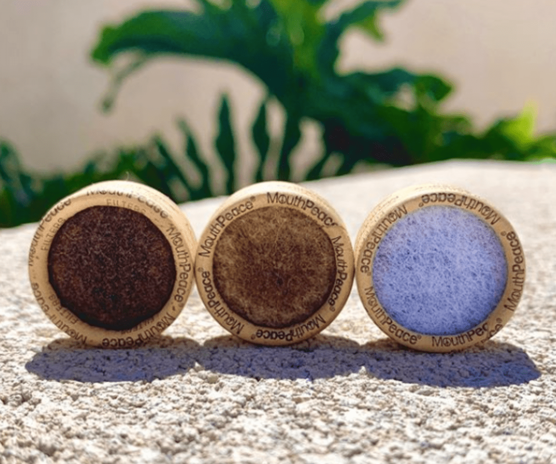 Three MouthPeace filters showing used brown residue next to a clean white filter on a stone surface.