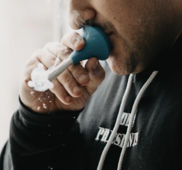 Person exhaling smoke through a blue handheld weed filter to ensure a cleaner, smoother smoking experience.
